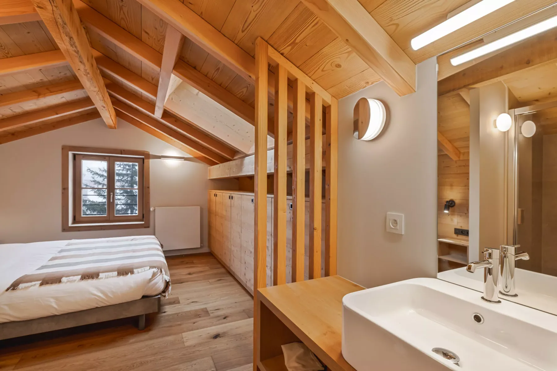 A loft bedroom with a bed, wooden beams, and a sink beside the mirror.