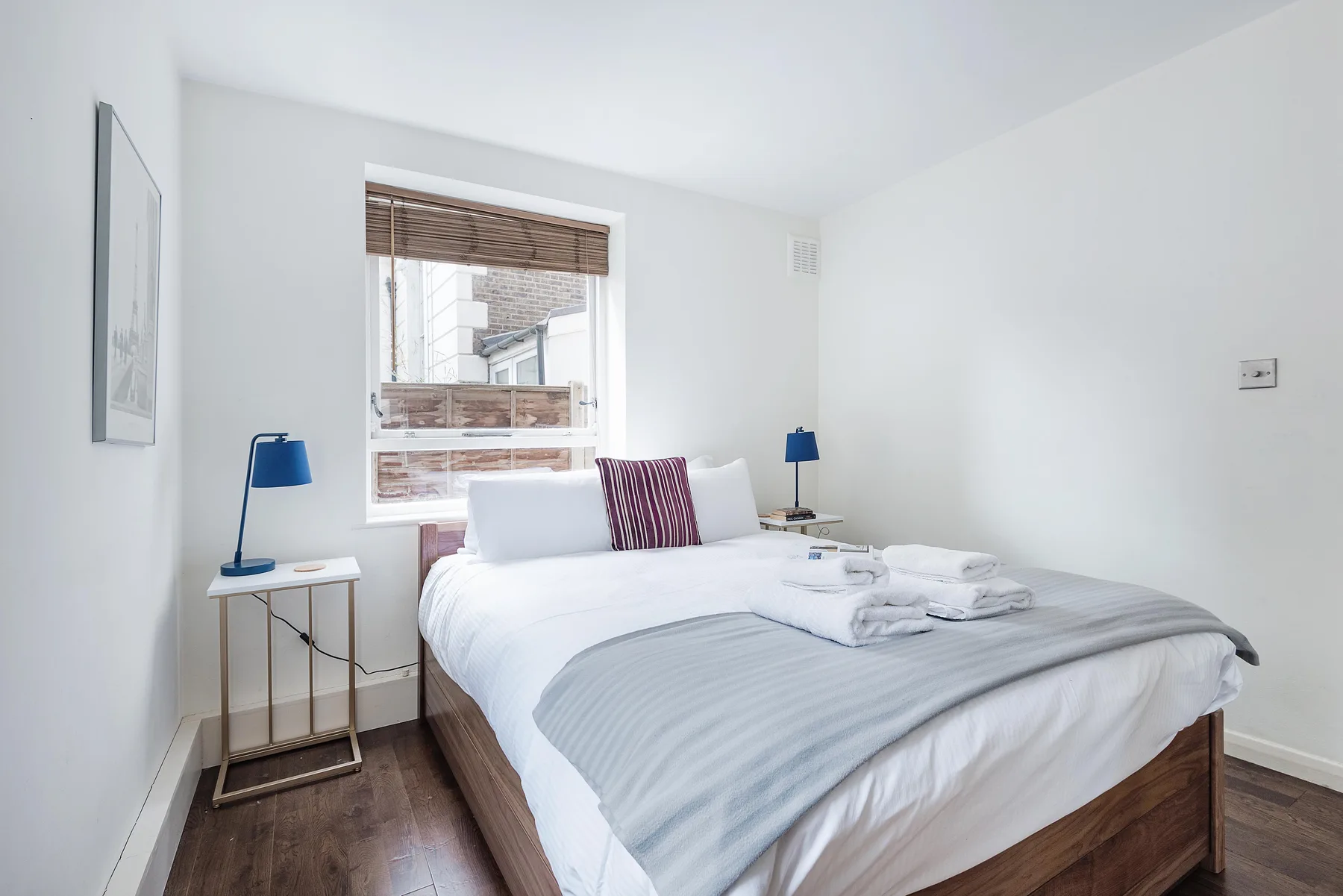Un dormitorio luminoso con una cama bien tendida y una ventana con persianas.
