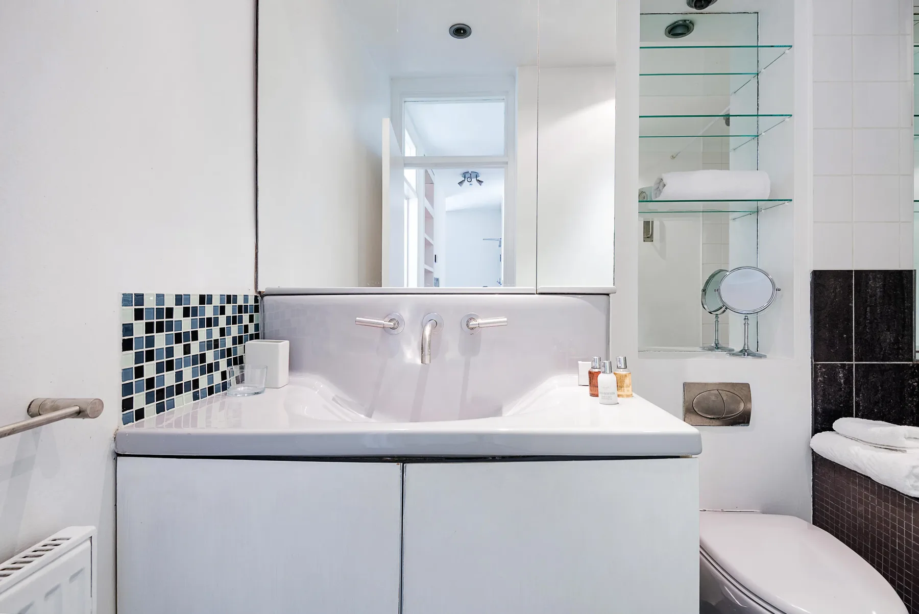 Un baño luminoso con bañera, lavabo y estantes de vidrio.
