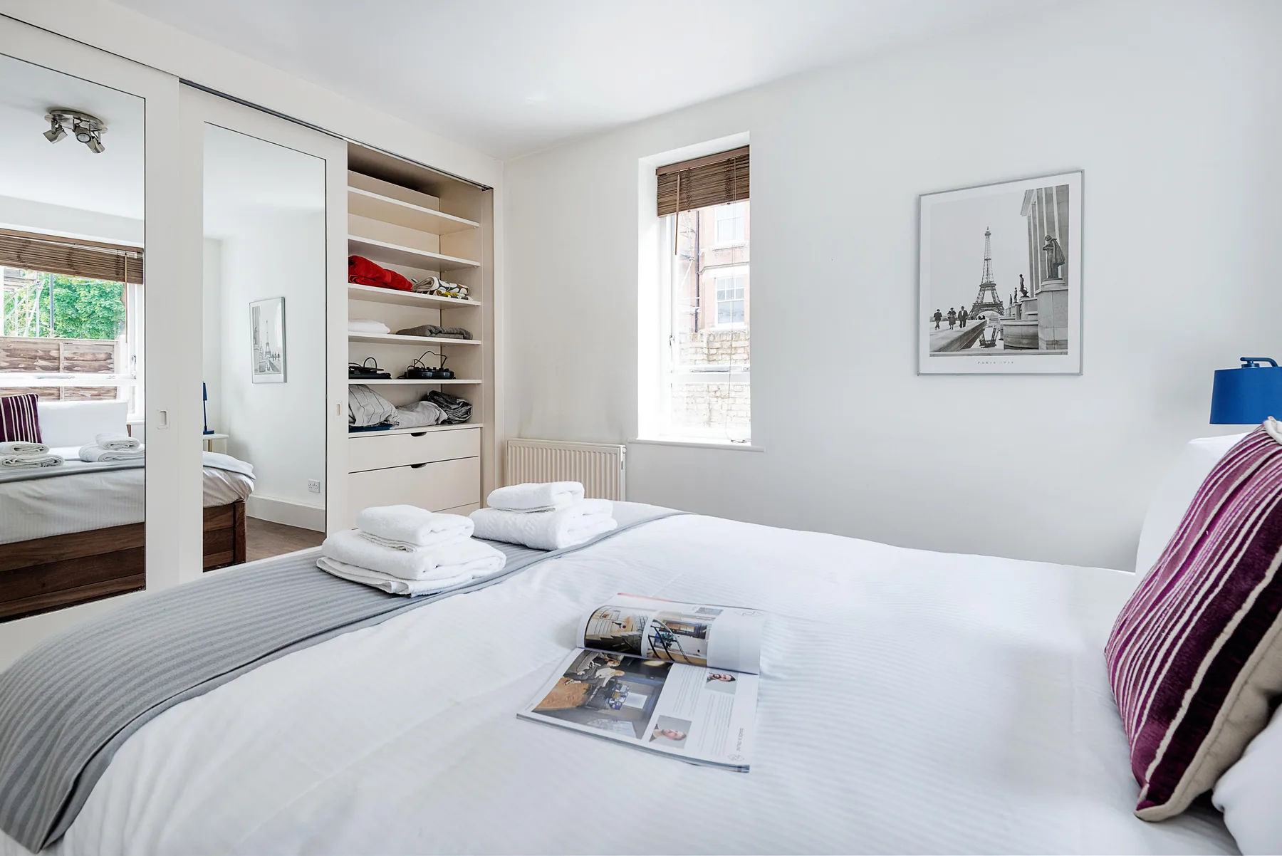 Un dormitorio luminoso con una cama tendida y estanterías abiertas.