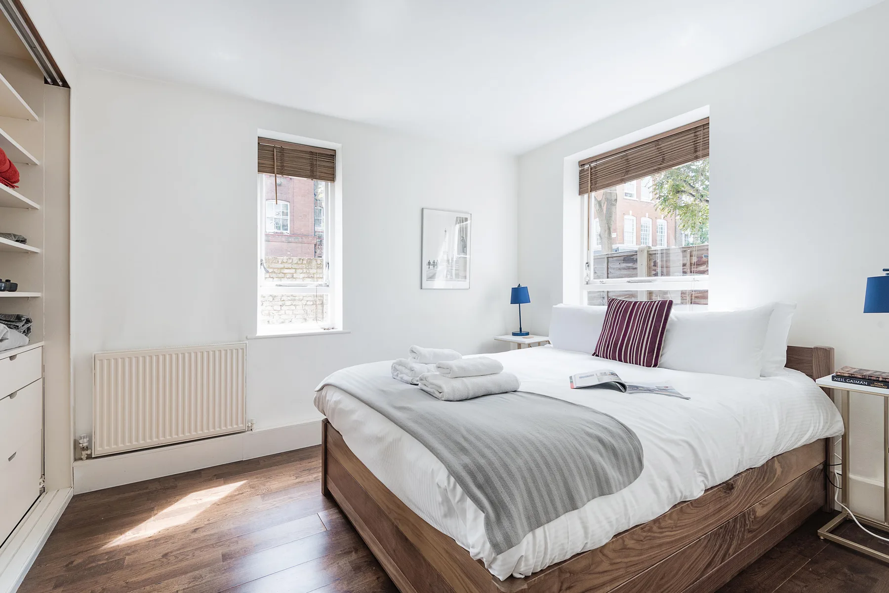 Un dormitorio luminoso con una cama grande y ventanas con vistas a edificios cercanos.