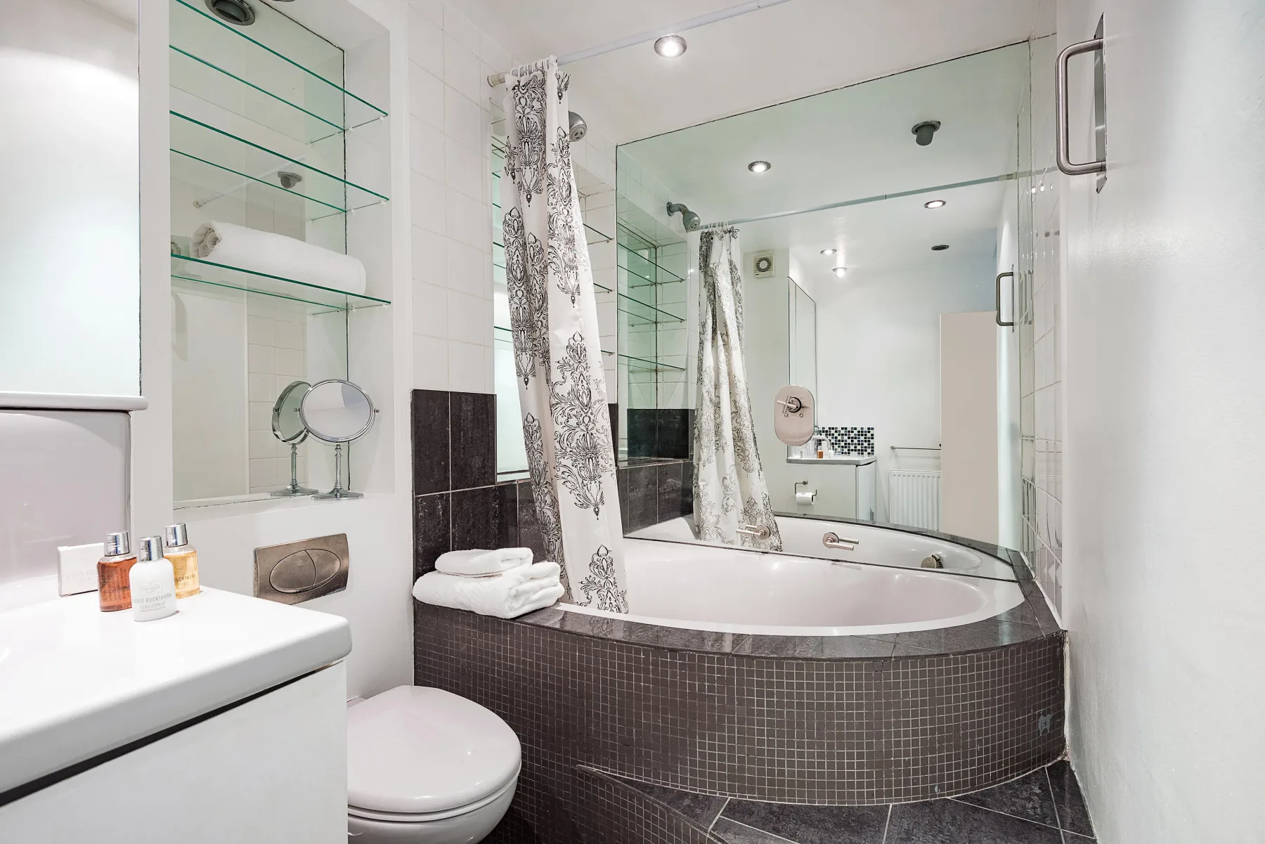 Un baño con bañera, cortinas estampadas y un gran espejo en la pared.