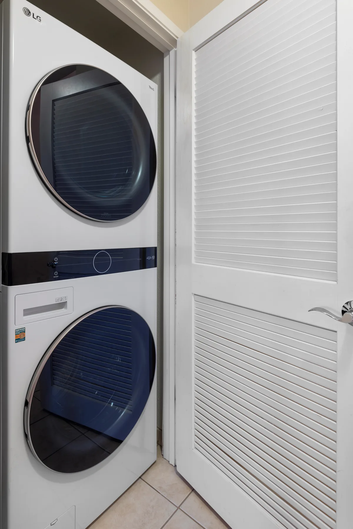 A stacked laundry appliance stands beside a white louvered door.