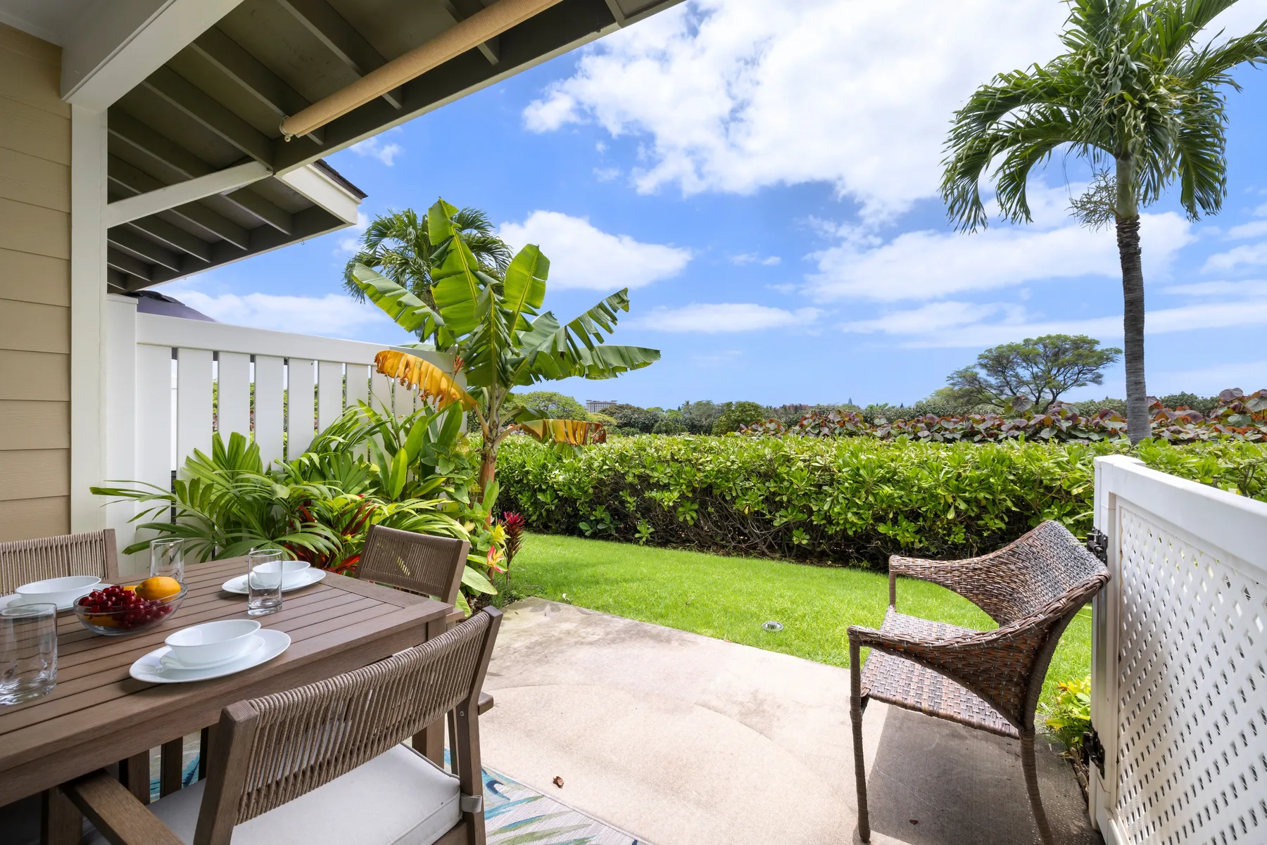 A covered outdoor dining area opens onto a green lawn, with tropical plants and seating.