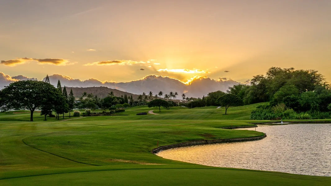 A green golf course borders a pond beneath a sunset sky.