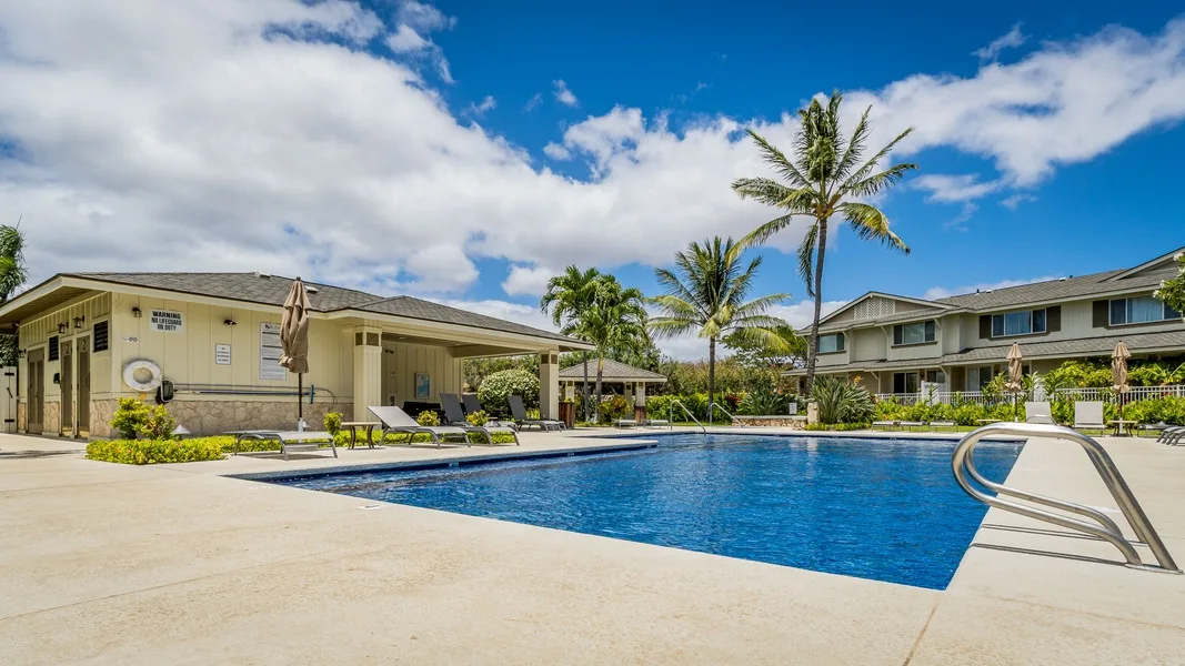 An outdoor swimming pool sits beside low-rise buildings and palm trees.