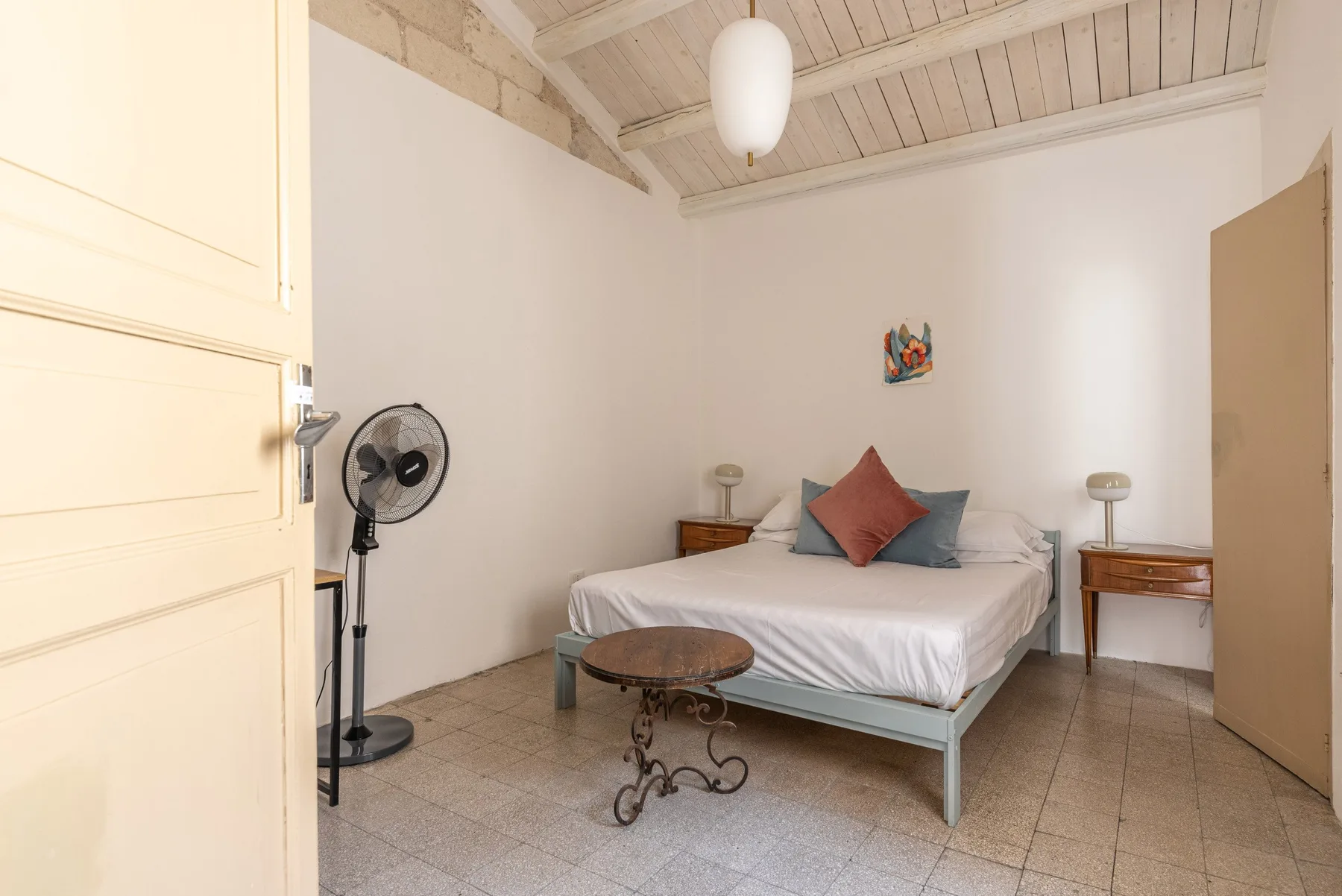 Un dormitorio con una cama, mesitas de noche y un ventilador de pie.