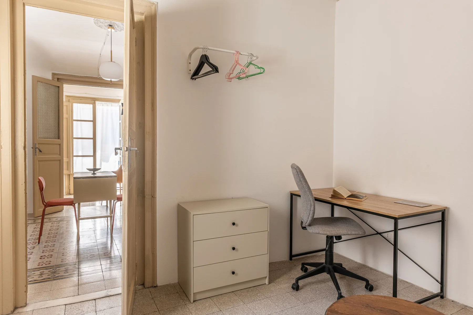 Un espacio de trabajo en un dormitorio con escritorio, silla y cómoda pequeña.