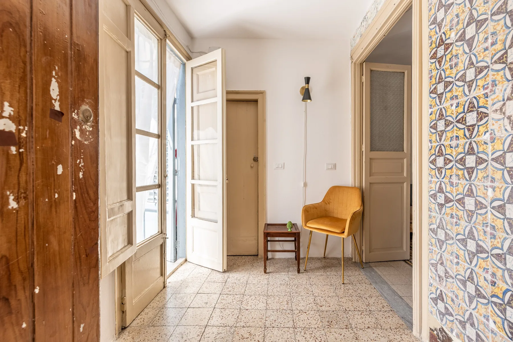 Un pasillo luminoso con paredes de azulejos estampados y una pequeña zona para sentarse.