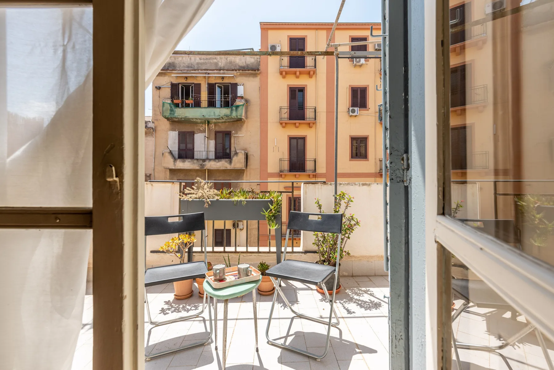 Un pequeño balcón con asientos y una mesa da a edificios de apartamentos vecinos.