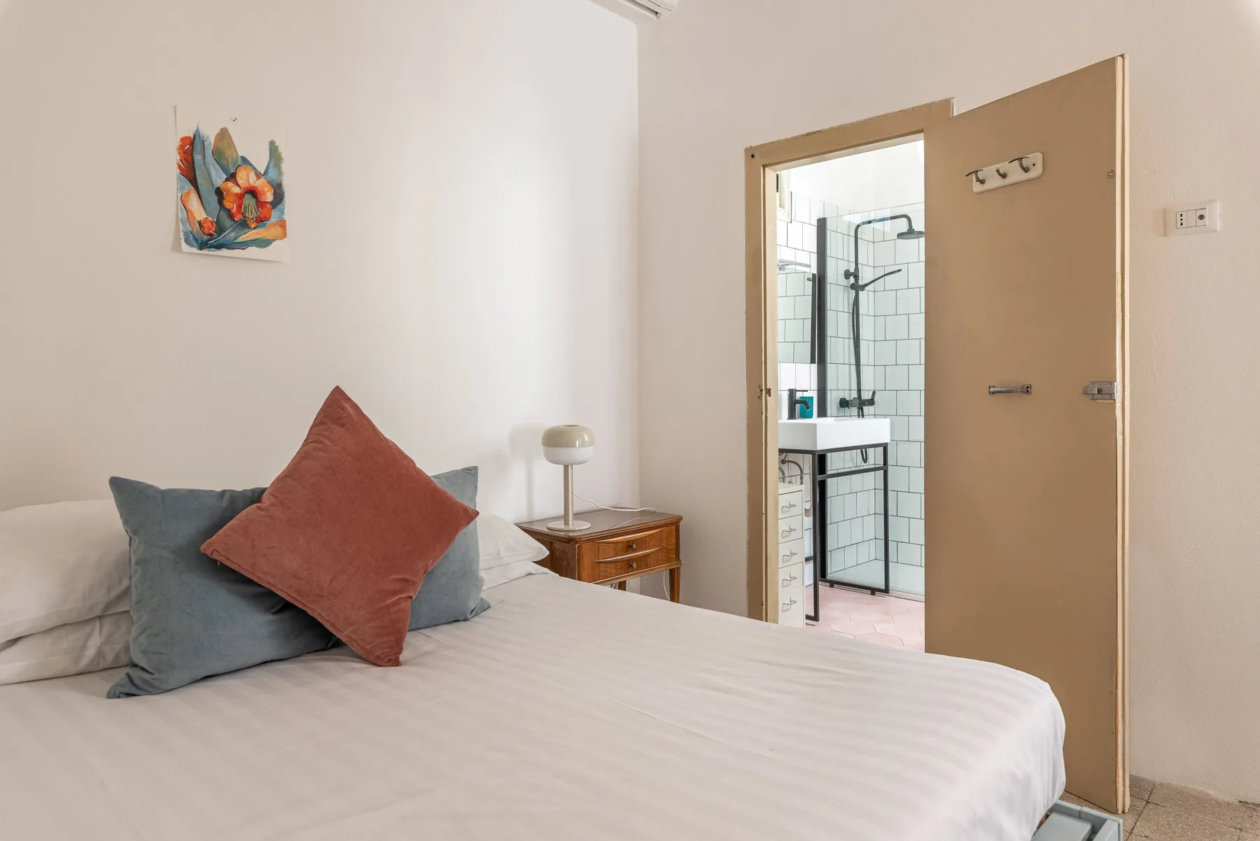 Un dormitorio con una cama y una puerta abierta que muestra una zona de ducha con azulejos.