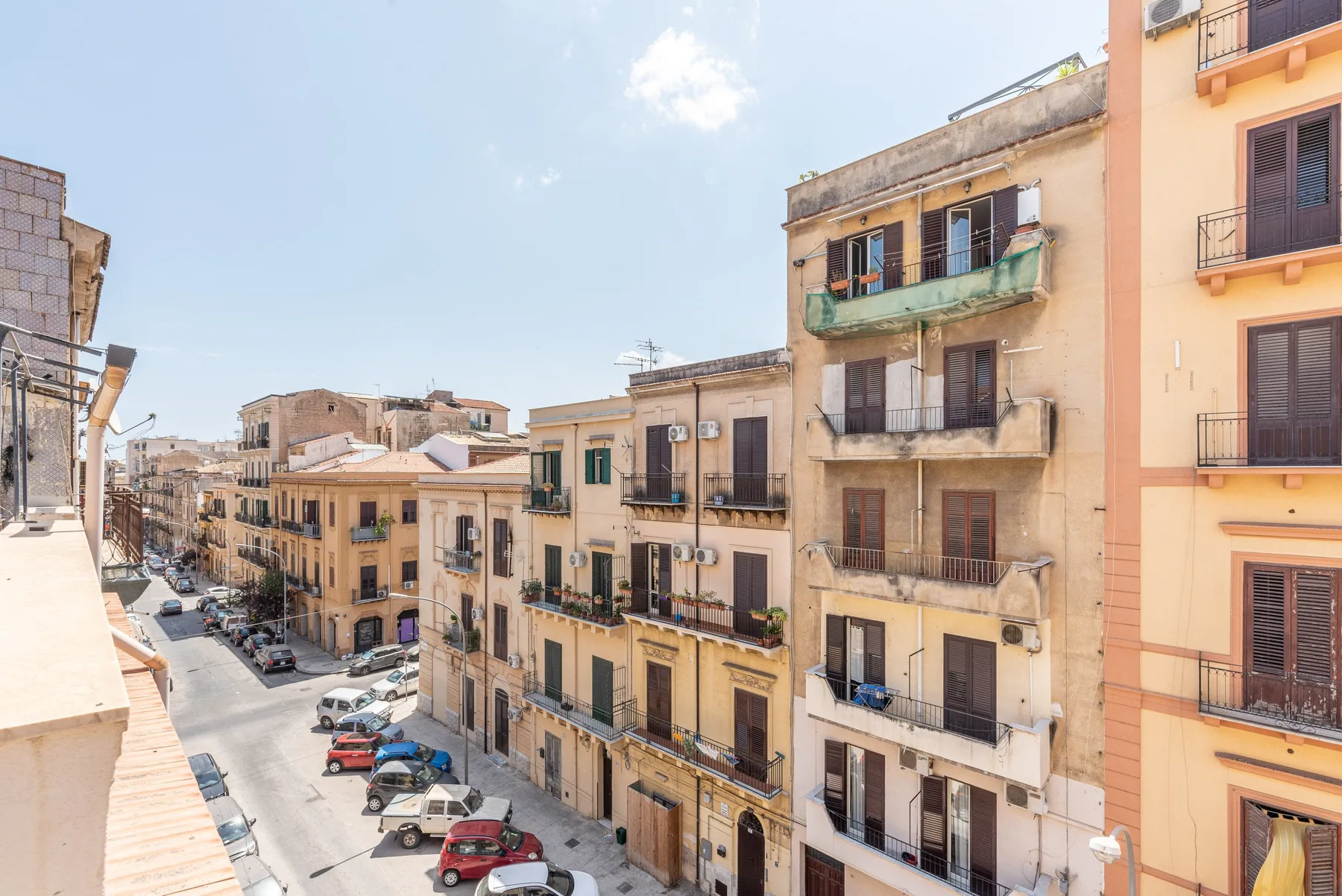 Una calle urbana bordeada de edificios residenciales y coches estacionados bajo un cielo despejado.