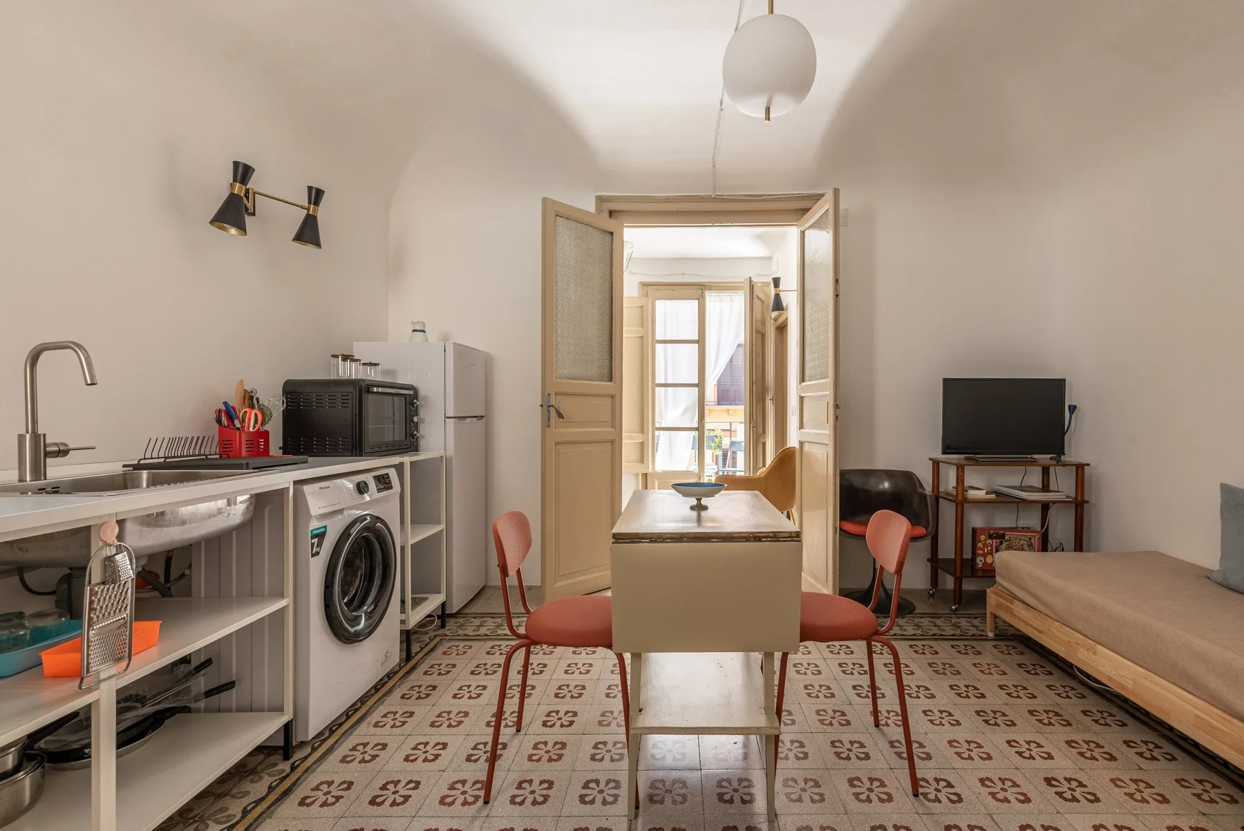 Una pequeña zona de estar y cocina tipo estudio con mesa, asientos y televisor.