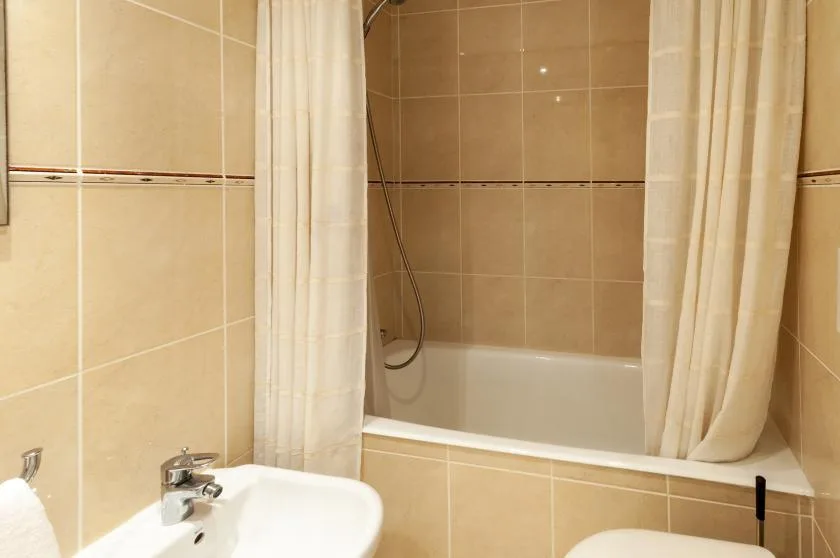 Un baño alicatado con bañera, cortina de ducha y lavabo.