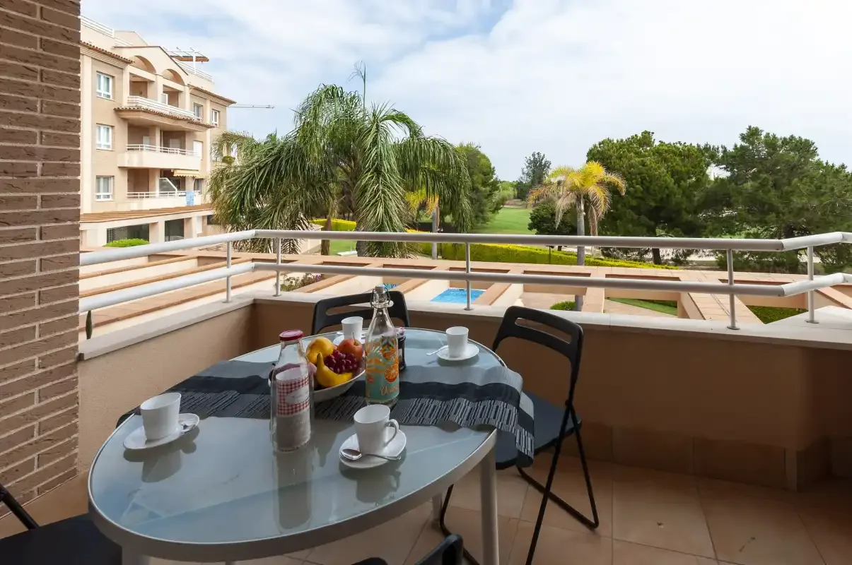 Una zona de estar en un balcón con una mesa frente a un patio ajardinado.