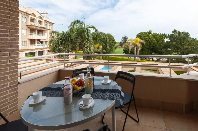 Una zona de estar en un balcón con una mesa, palmeras y una piscina a la vista.