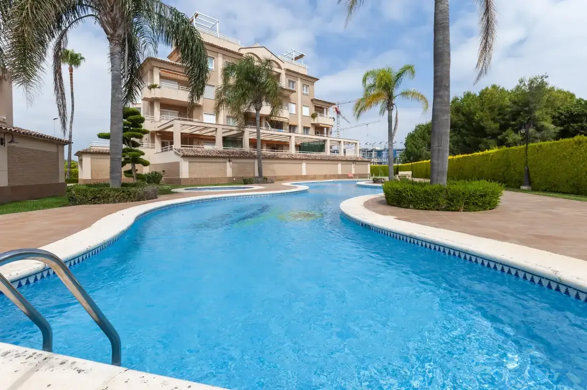 Una piscina al aire libre se curva entre jardines junto a un edificio de apartamentos.