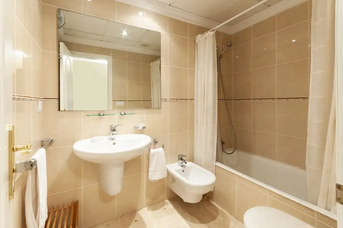 Un baño alicatado con lavabo, inodoro y bañera con cortina de ducha.