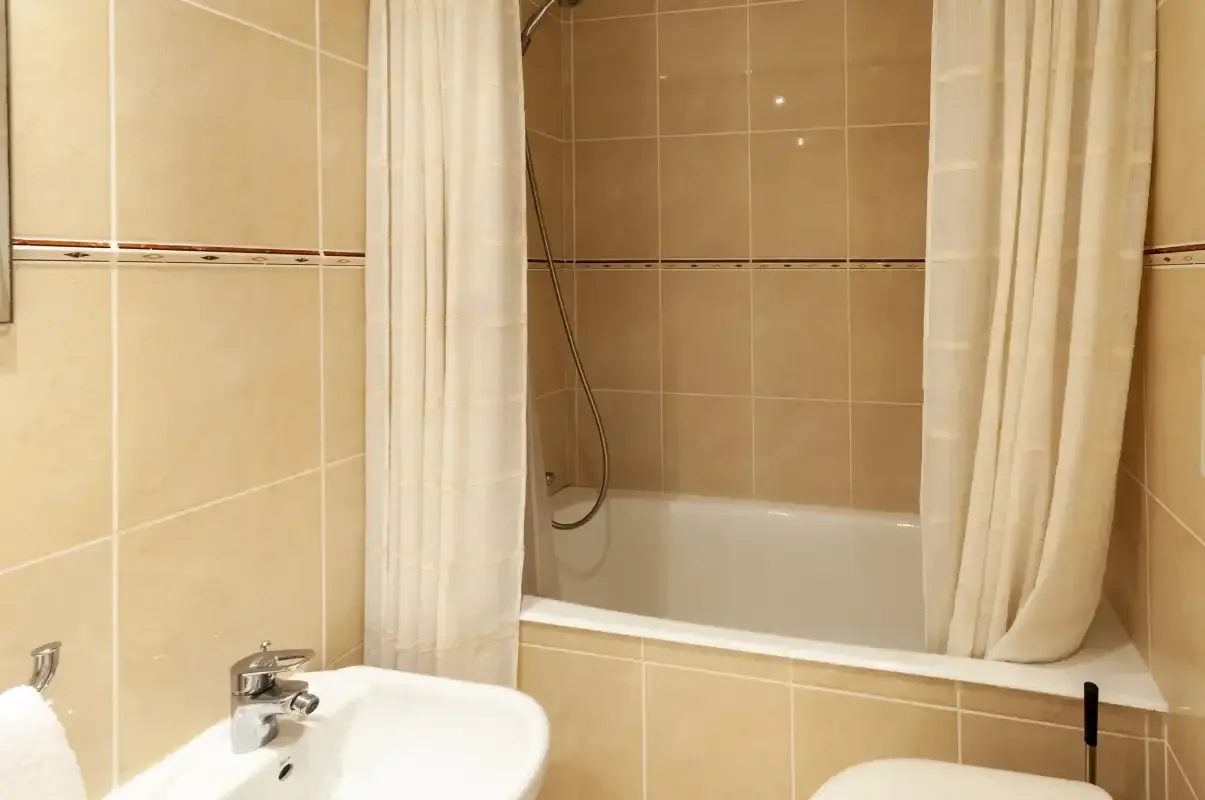 Un baño alicatado con una bañera detrás de una cortina.