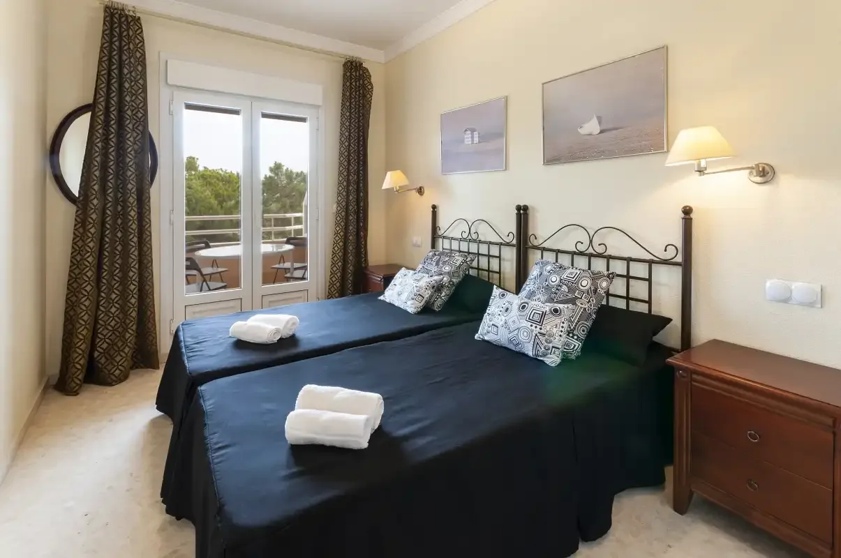 Un dormitorio con dos camas, cojines estampados y puertas de cristal que dan a un balcón.