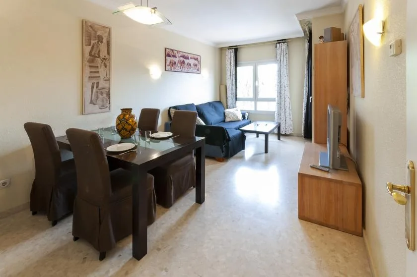Una sala de estar y comedor con una mesa, asientos y un sofá junto a la ventana.