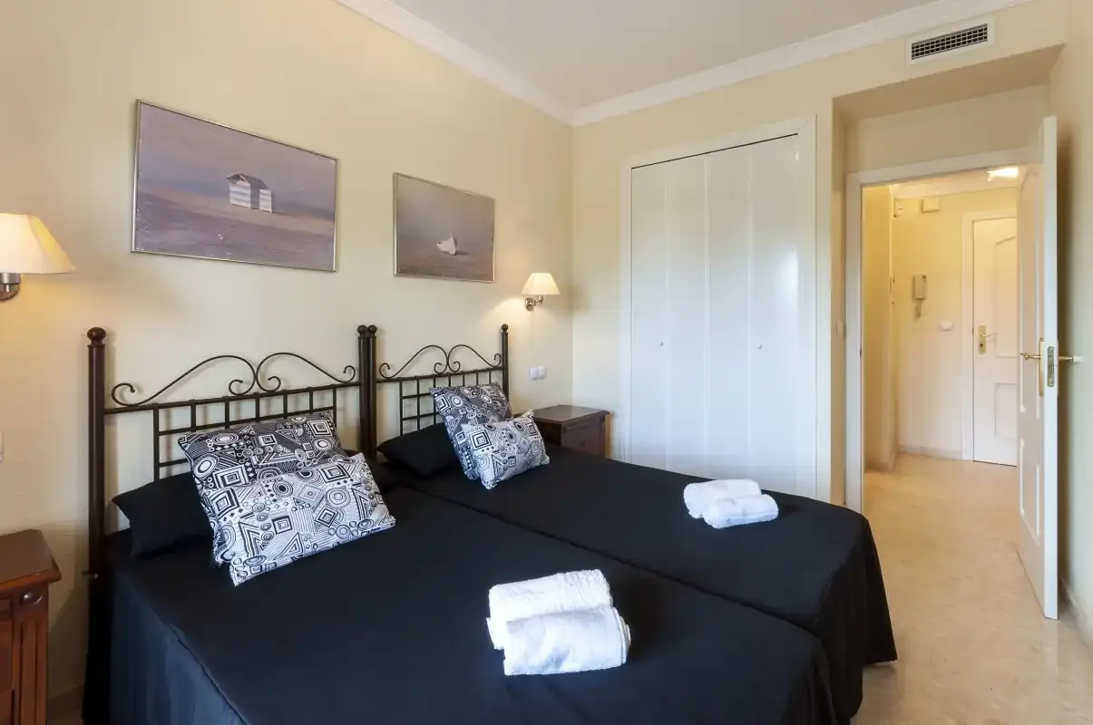 Un dormitorio con dos camas, almohadas estampadas y una puerta abierta al baño.