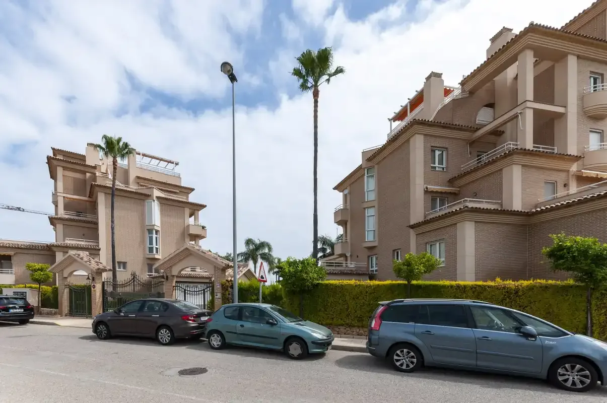 Edificios de apartamentos bordean una calle con coches estacionados y palmeras.