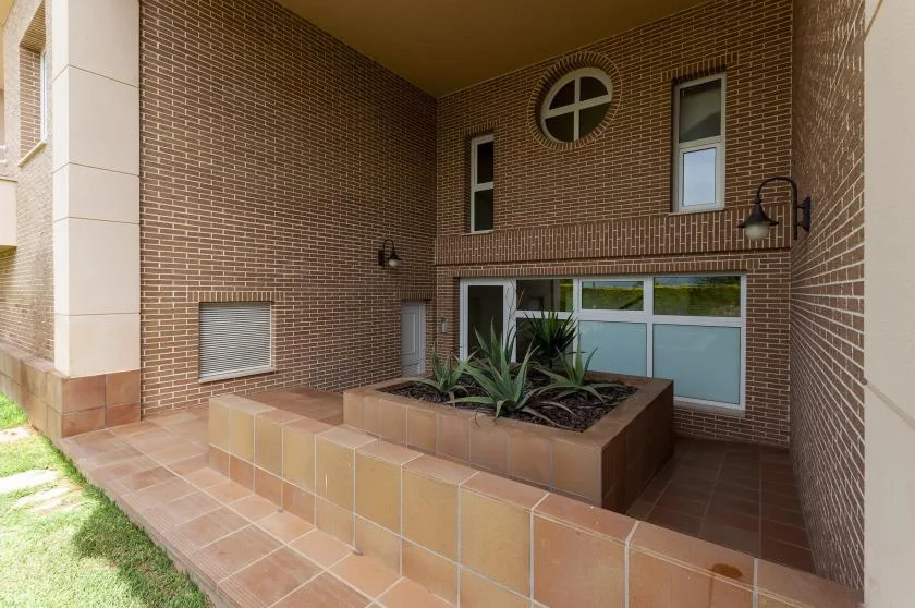 Un patio cubierto de ladrillo tiene una jardinera elevada con plantas frondosas.