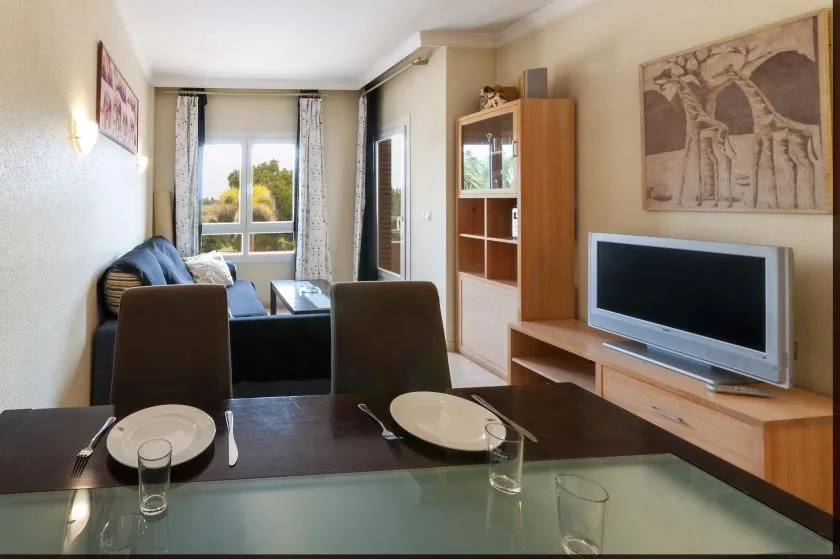 Una zona de estar y comedor con televisor, asientos y una ventana.