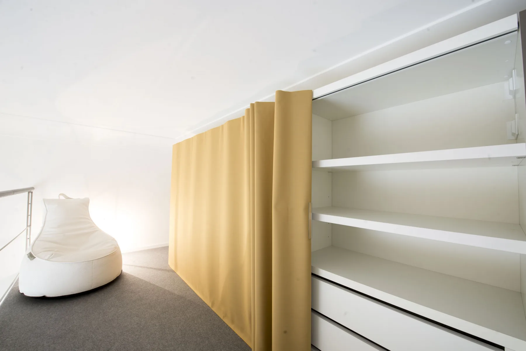 Una habitación luminosa con estantes blancos y una fila de cortinas doradas.
