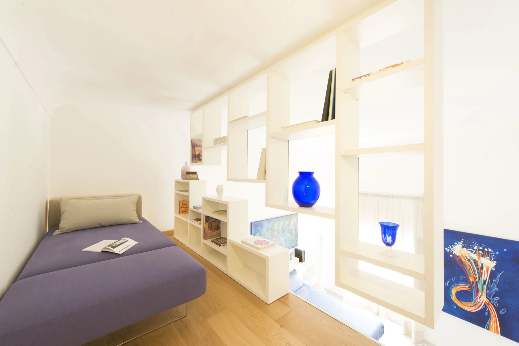 Un dormitorio compacto con una cama junto a una luminosa estantería empotrada.