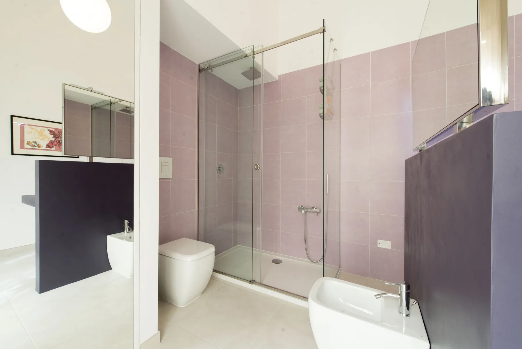 Un baño con ducha de vidrio y paredes de azulejos rosa claro.
