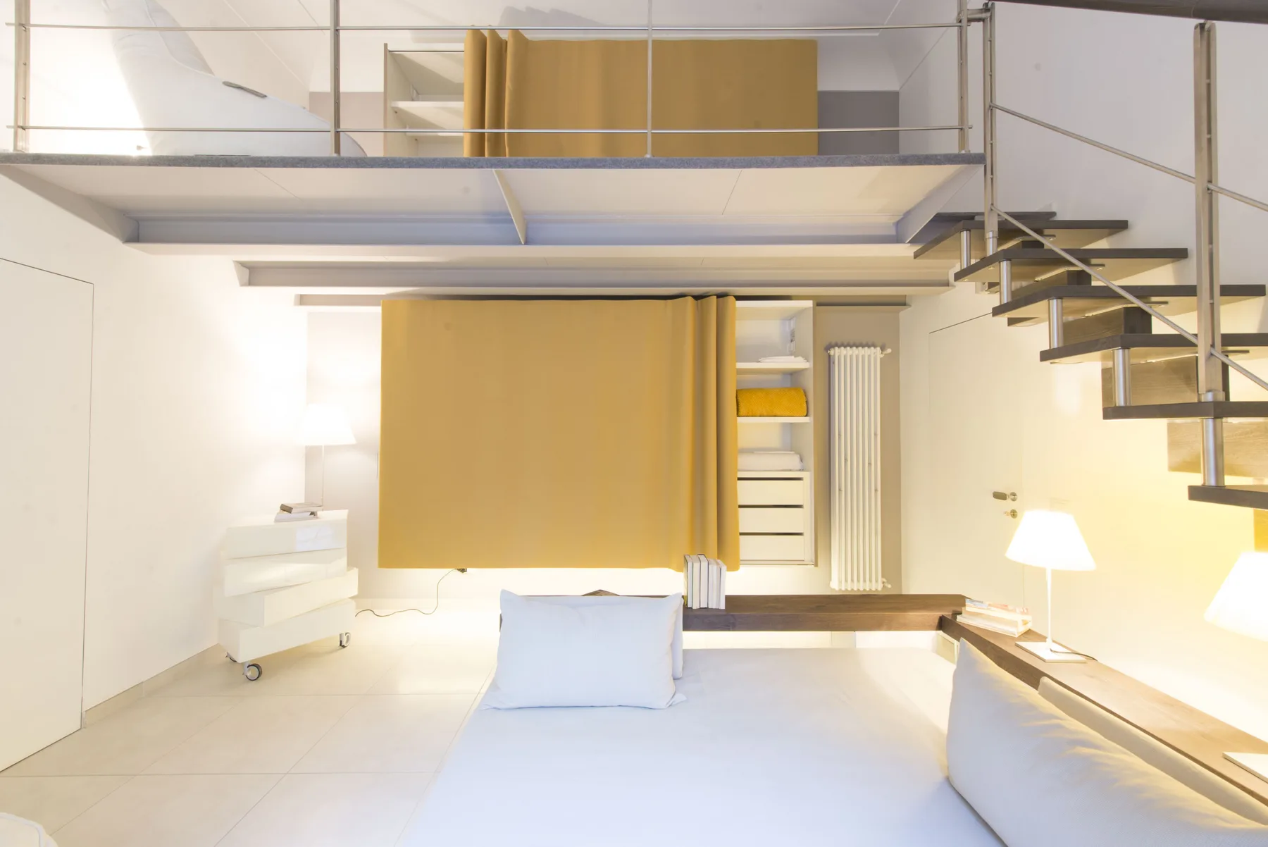 Un dormitorio luminoso con una cama bajo un altillo elevado y una escalera.