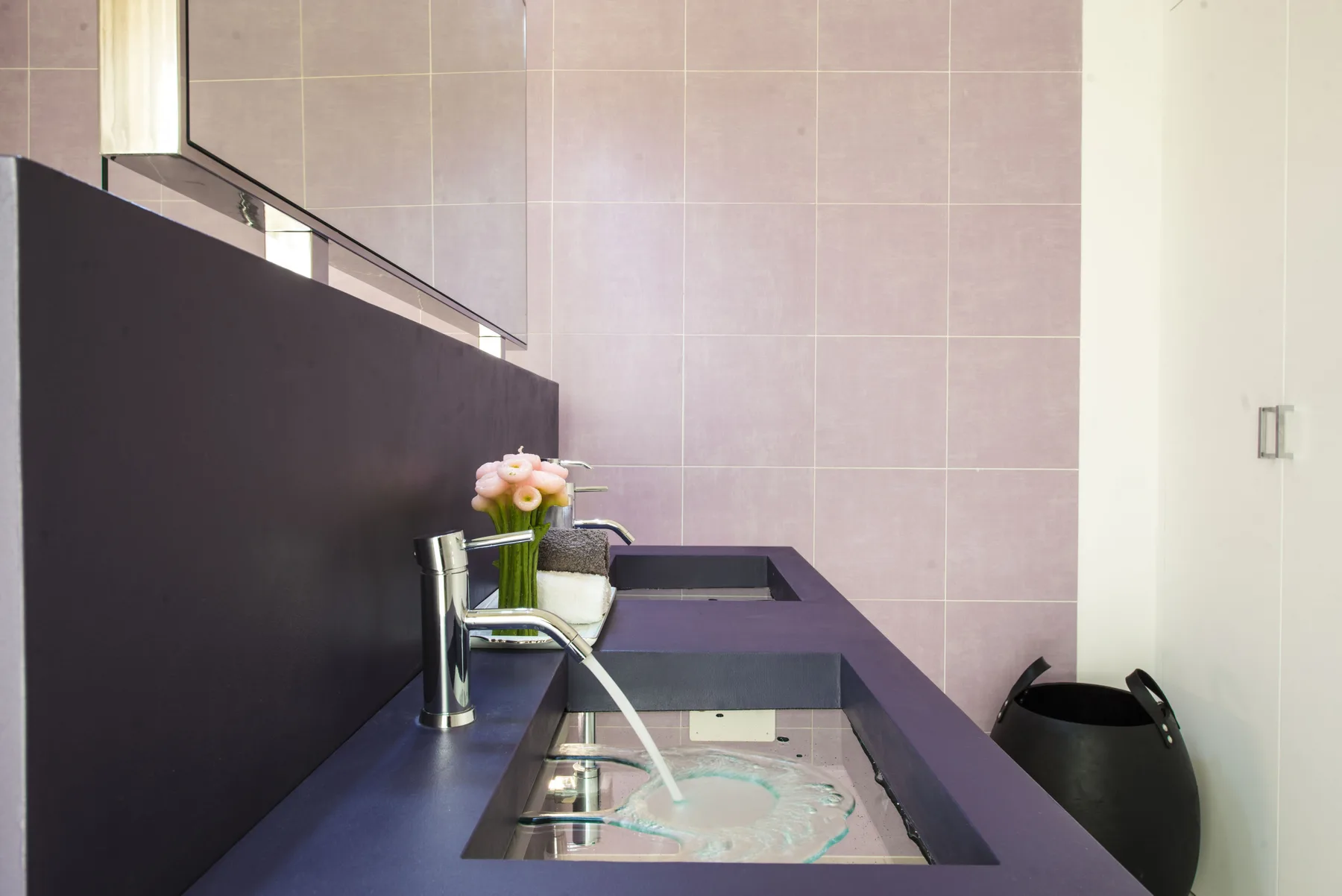 Un mueble de baño moderno tiene un lavabo alargado y flores rosadas.