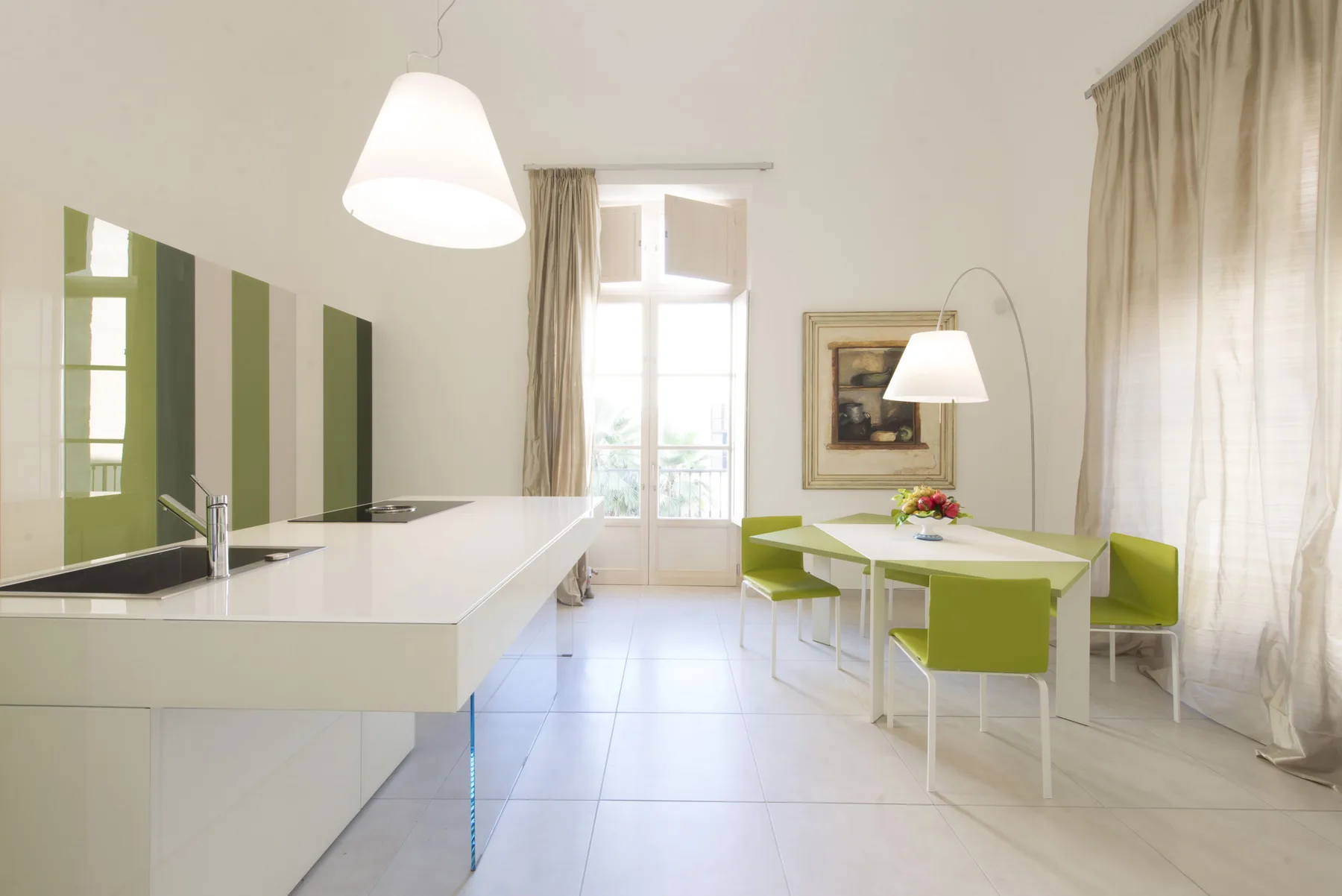 Comedor luminoso con una mesa blanca, asientos verdes y una isla de cocina.