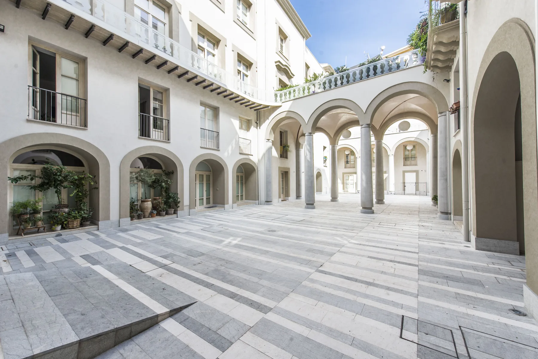 Un patio luminoso con pasillos de arcos y un suelo de franjas de piedra.