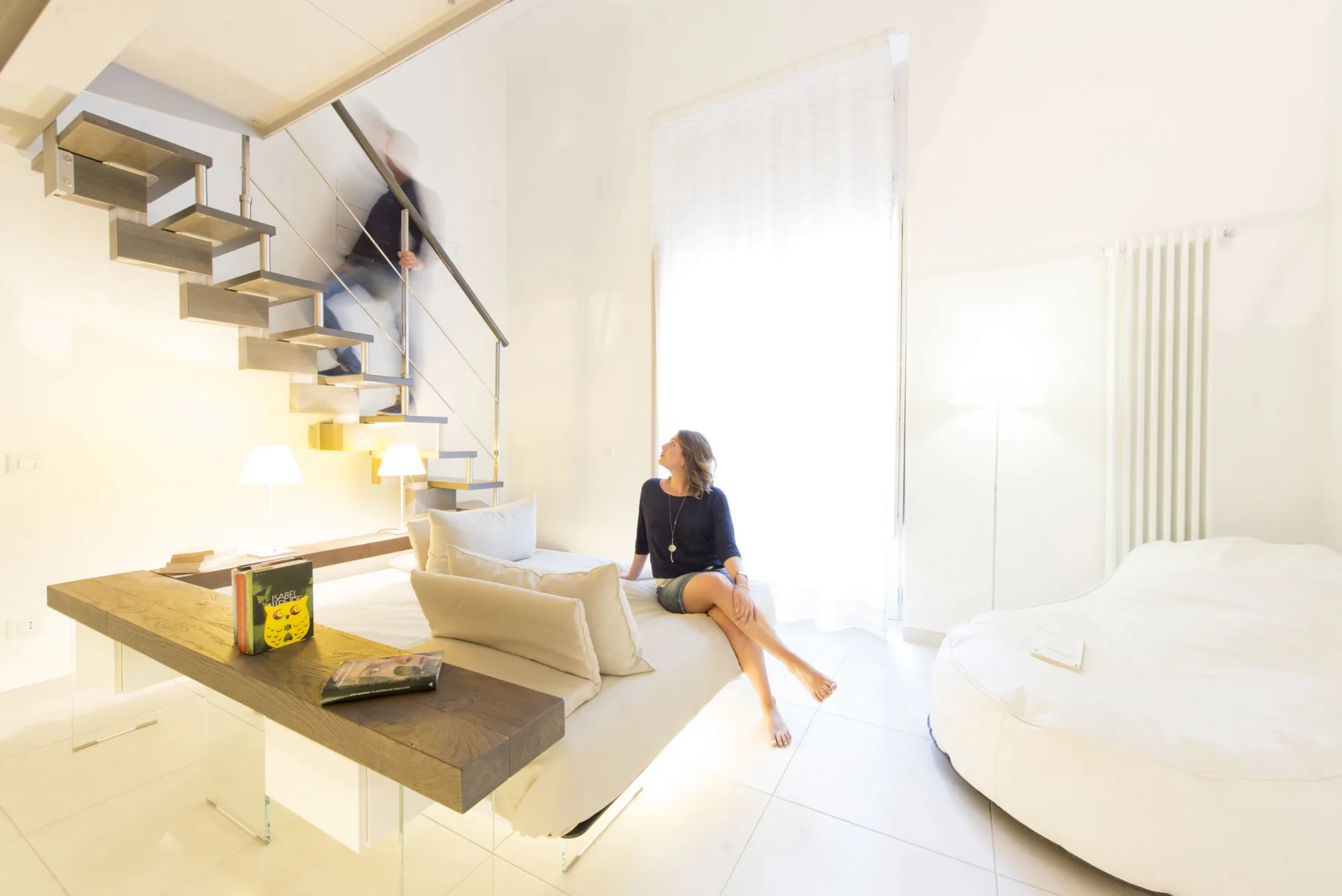 Un dormitorio luminoso con una cama elevada, un escritorio y una persona sentada cerca.