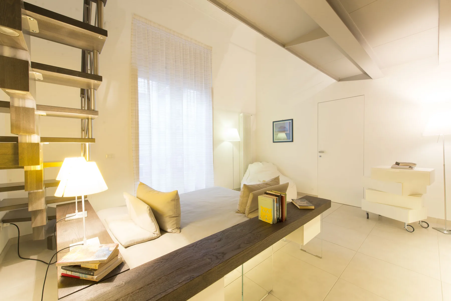 Un dormitorio luminoso con cama, lámpara de noche y estanterías junto a una pared.
