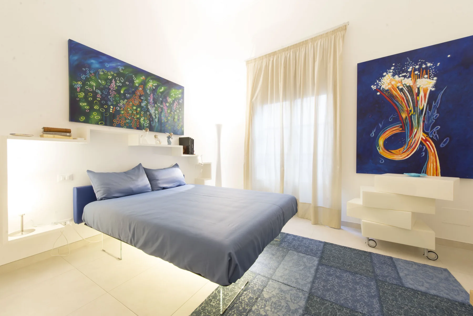 Un dormitorio luminoso con una cama gris, arte colorido en las paredes y una alfombra estampada.