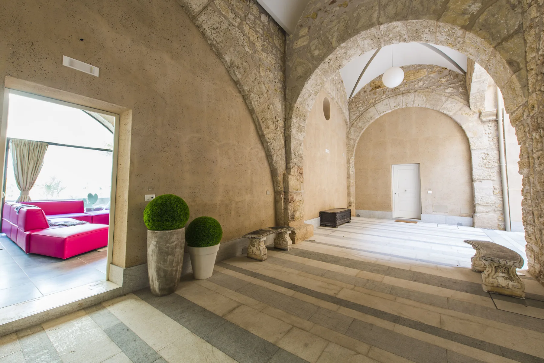 Un interior de piedra con arcos se abre a una estancia luminosa con asientos rosas.