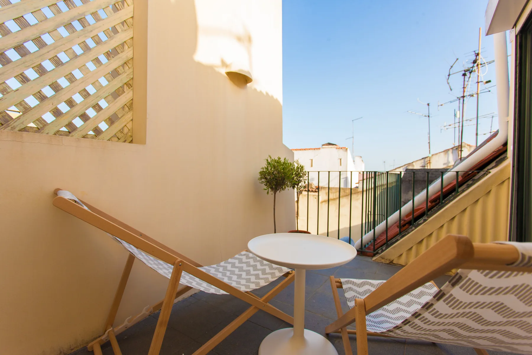 Una terraza soleada con asientos, una mesa pequeña y una planta en maceta.