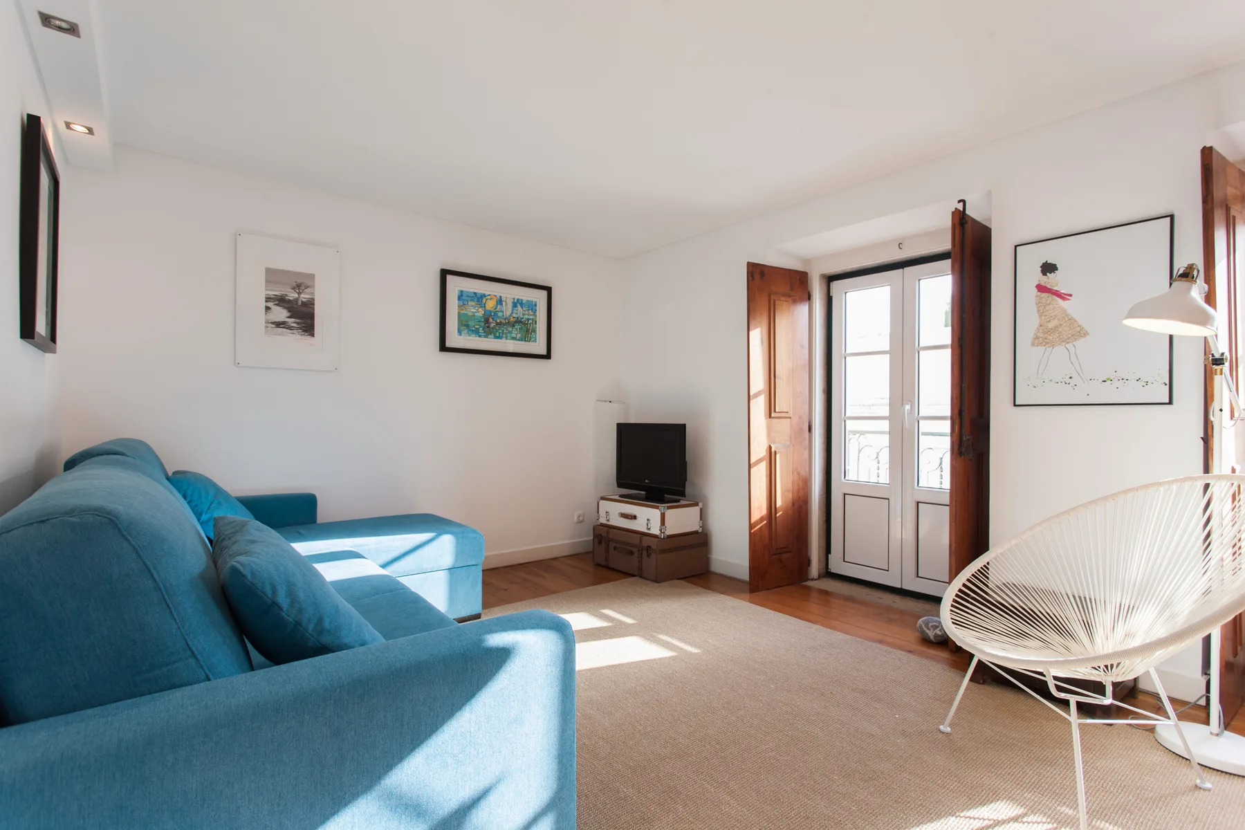A bright living room with blue seating, framed artwork, and glass doors.