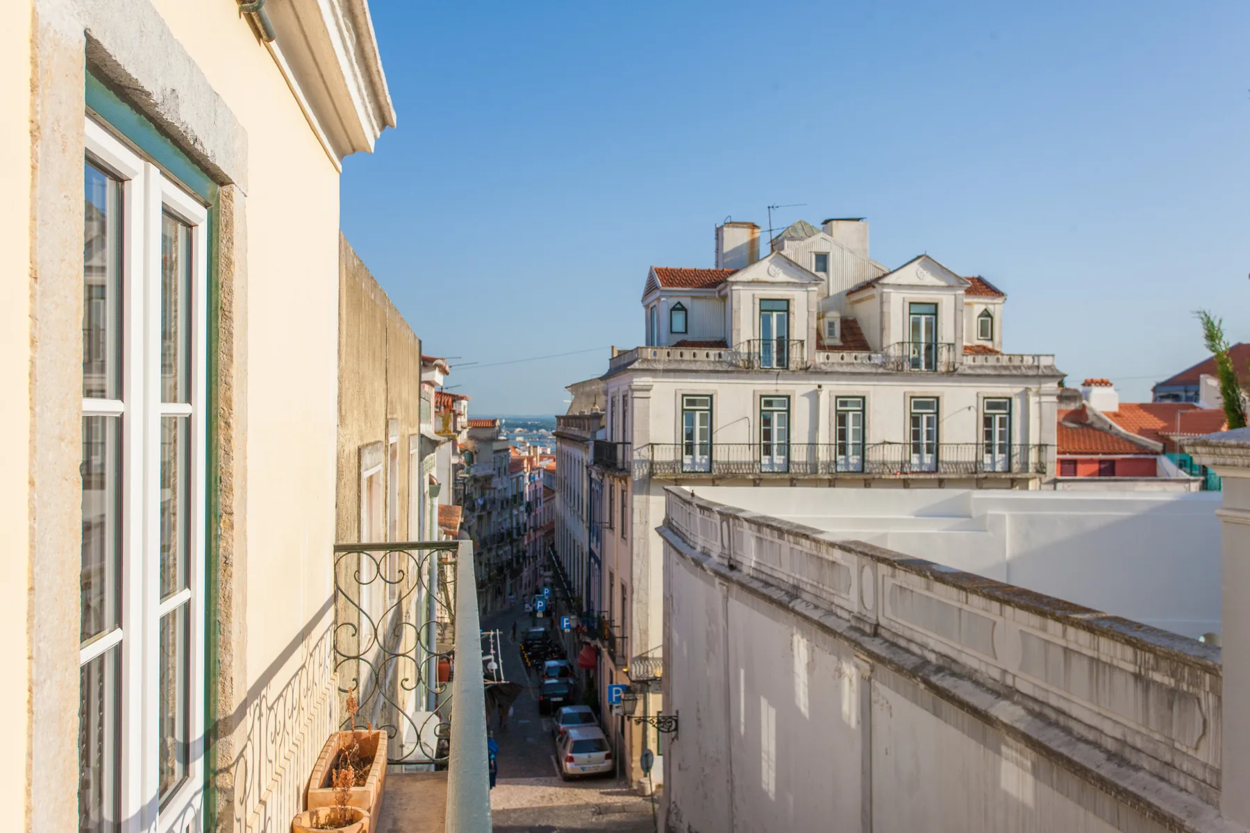 A narrow city street is seen between nearby buildings, with a distant glimpse of water.