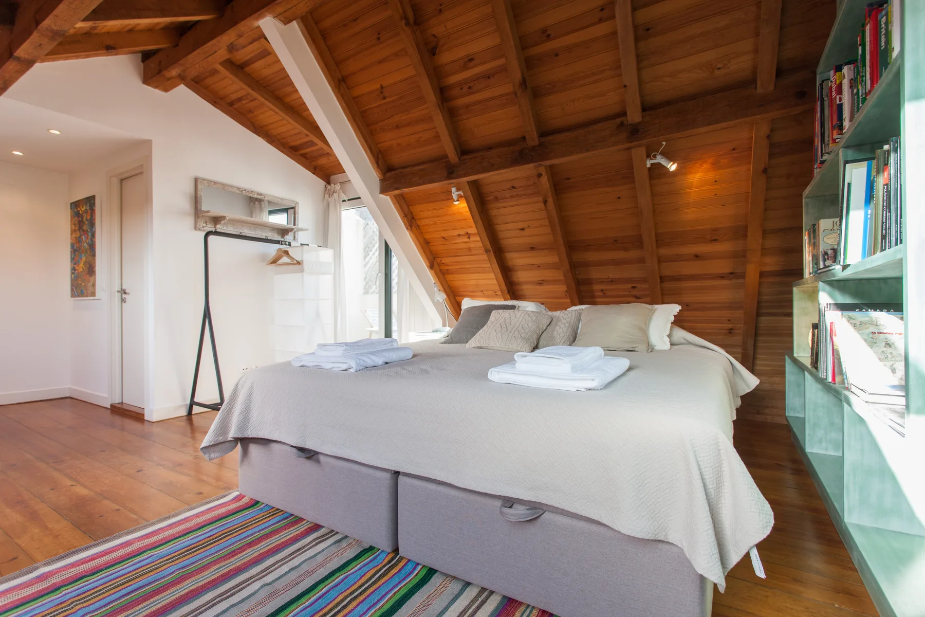 A bedroom with a large bed, folded towels, and a sloped wooden ceiling.