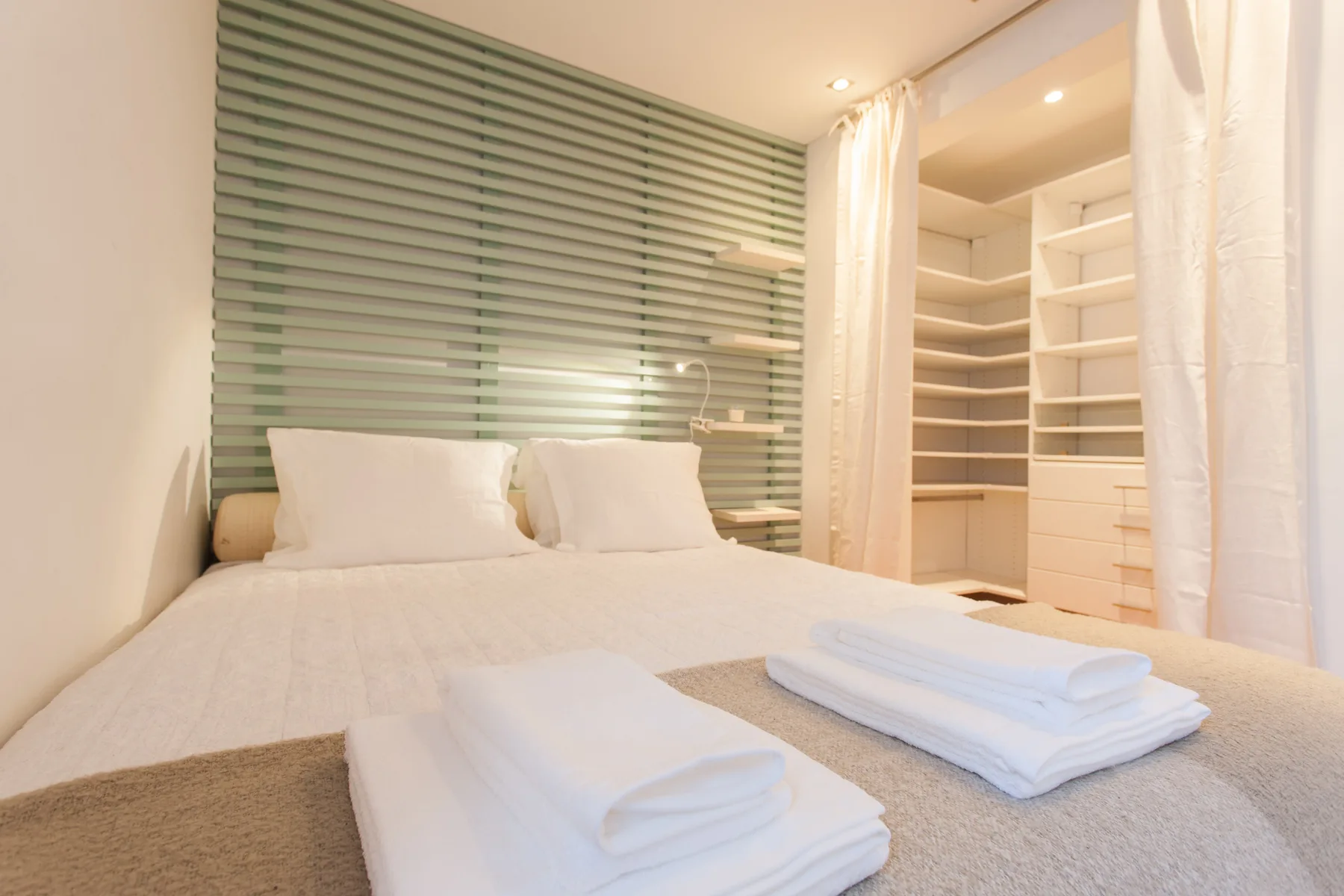 A bedroom with a bed and folded towels beside open shelving.