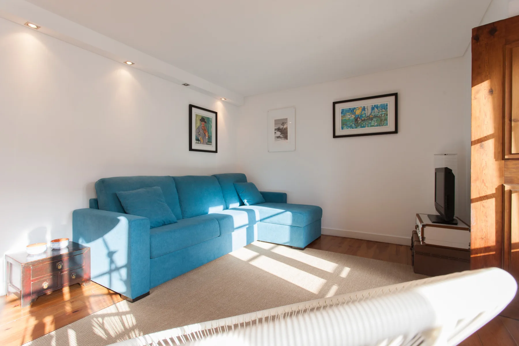 A bright living room with blue seating, framed artwork, and a television.