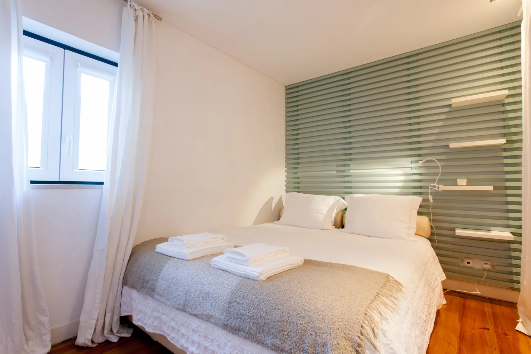 A bedroom with a neatly made bed beside a large window.