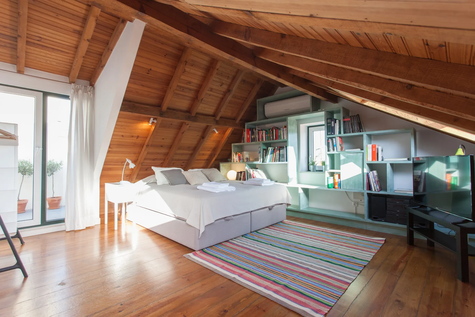 Un dormitorio tipo loft luminoso con cama, alfombra colorida y estanterías.