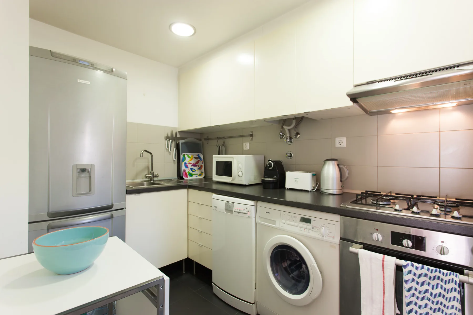 Una cocina luminosa con refrigerador, pequeños electrodomésticos y una lavadora.