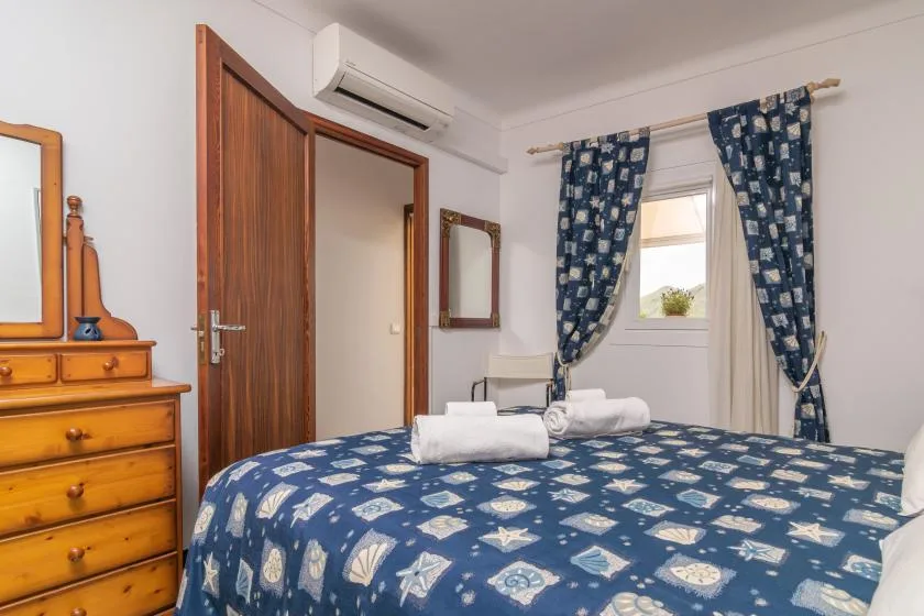 A bedroom with blue patterned bedding, tied-back curtains, and a wooden dresser.